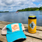 Day Drinkin' turquoise trucker hat on a dock beside the water, perfect for patio pints, summer adventures, and spontaneous afternoons